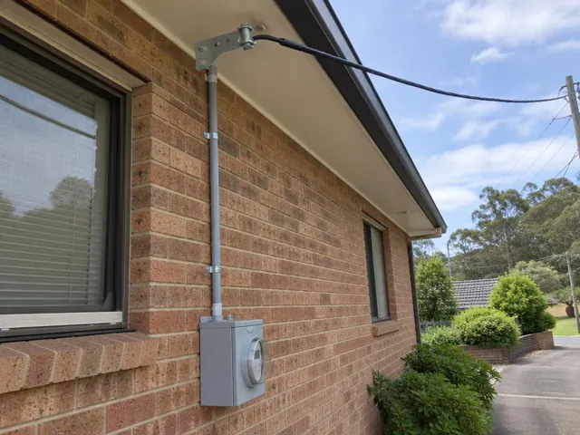 Brick house exterior with new overhead service cable, point-of-attachment bracket and meter box in Belrose